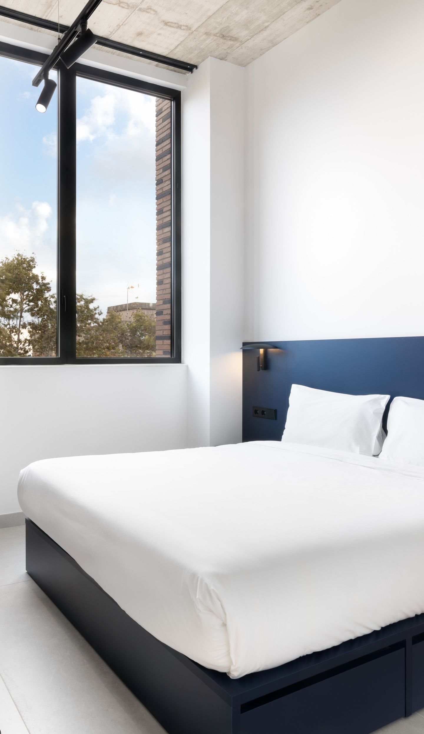Modern bedroom with a double bed, white bedding, navy headboard and a large window