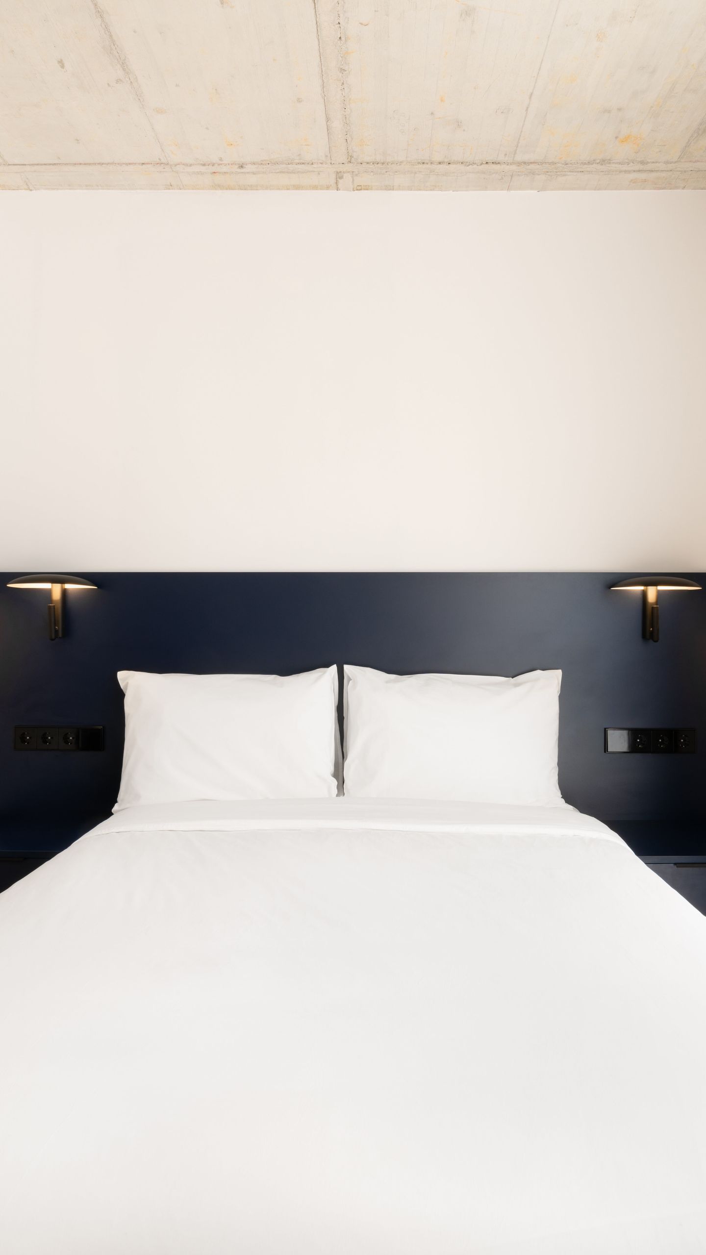 Cama con ropa de cama blanca, almohadas blancas y cabecero oscuro con apliques de pared.