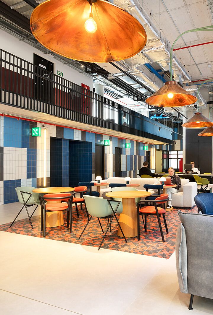 Modern interior room with tables, chairs and pendant lamps, with people in the background.