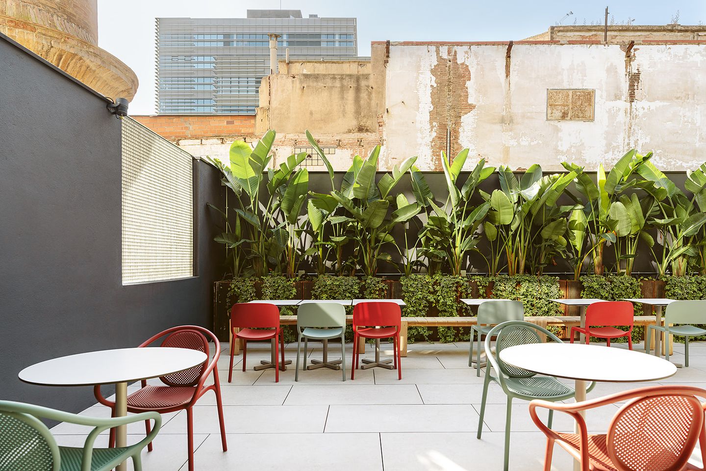 Terraza con mesas redondas, sillas de colores y plantas tropicales.