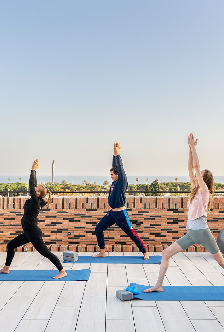 Tres personas hacen yoga en una terraza frente al mar.