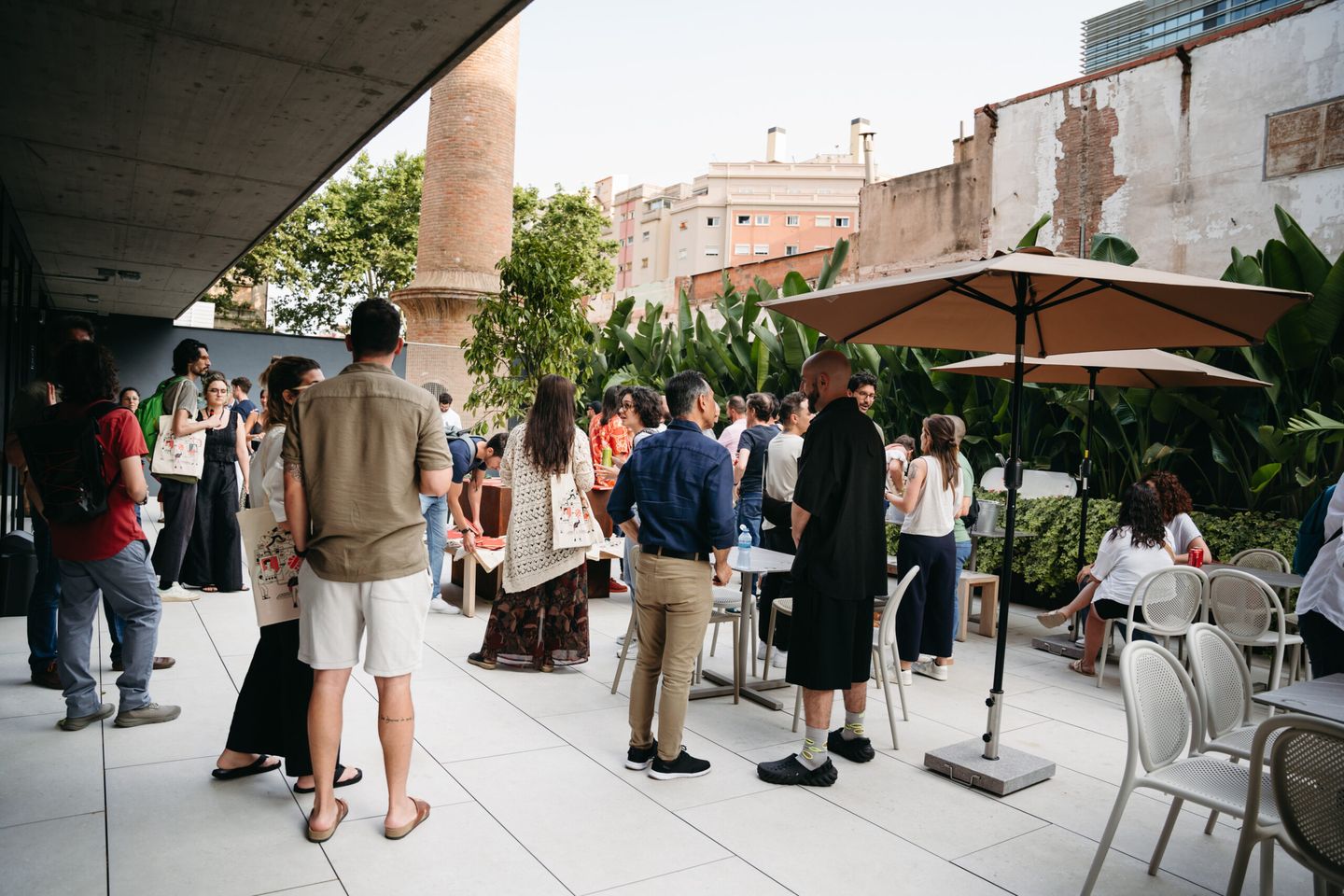 Personas reunidas en una terraza al aire libre con sombrillas y plantas.