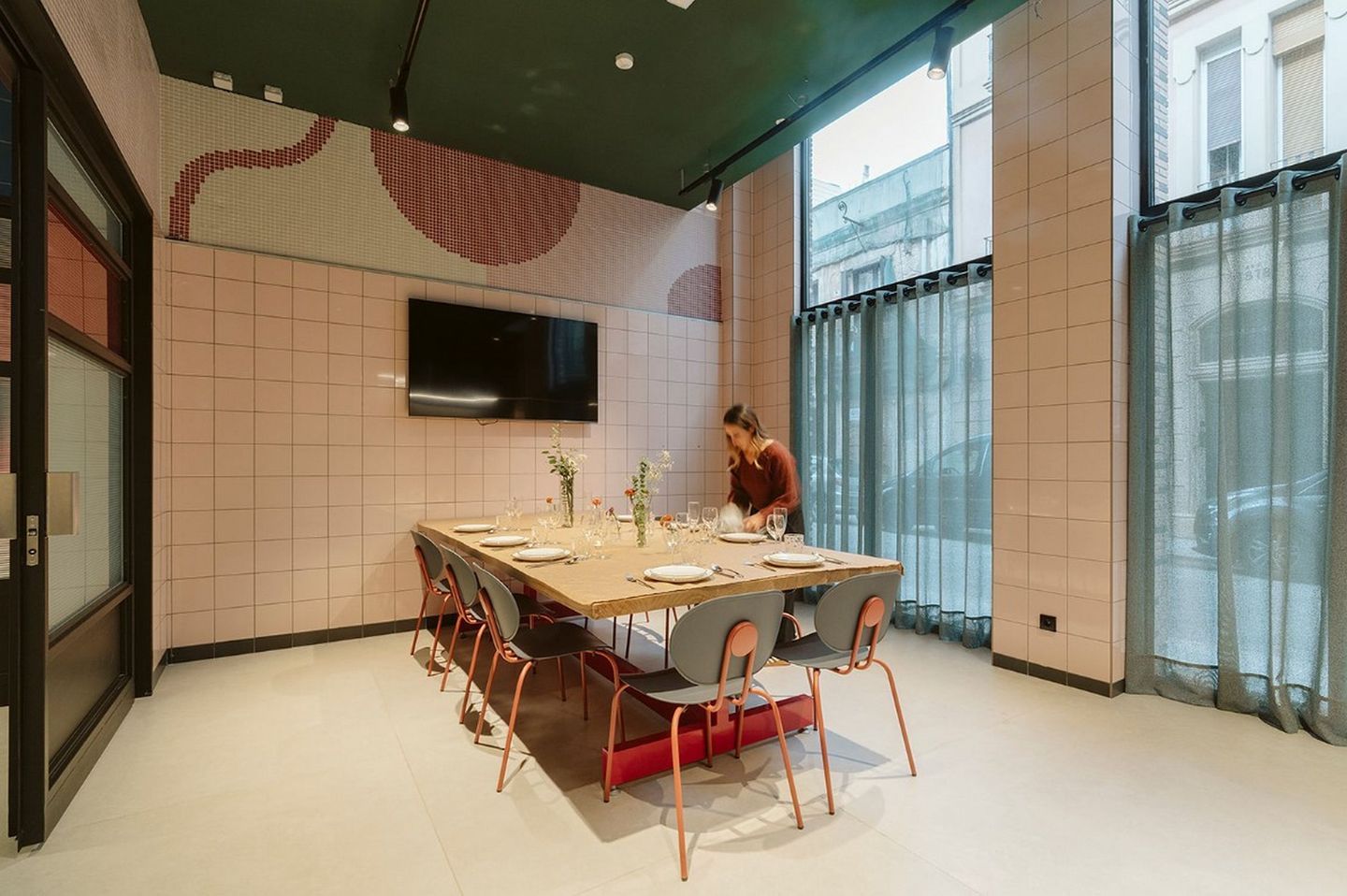 Dining room with a set table, wall screen and a person arranging place settings.