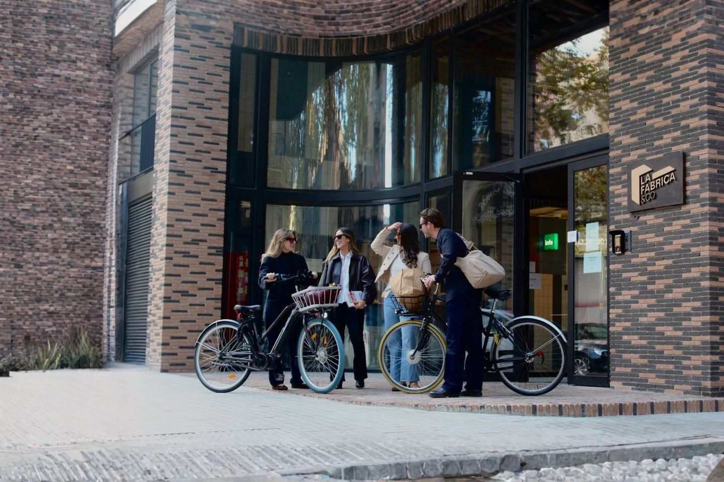 Cuatro personas conversan junto a varias bicicletas delante de un edificio de ladrillo.