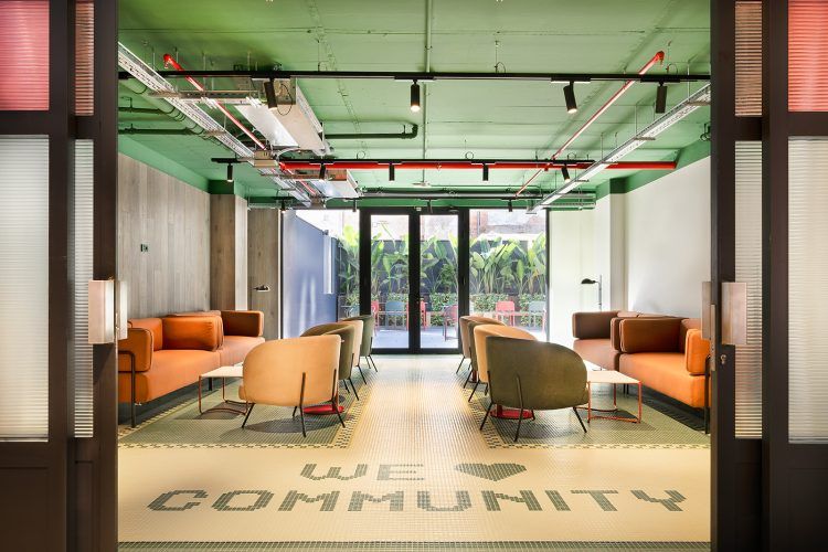 Salón moderno con sofás naranjas, sillones, un techo verde y suelo con texto que dice WE ♥ COMMUNITY.