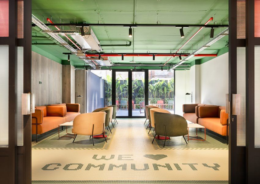 Sala de reuniones moderna con sofás naranjas, sillas y techo verde industrial.