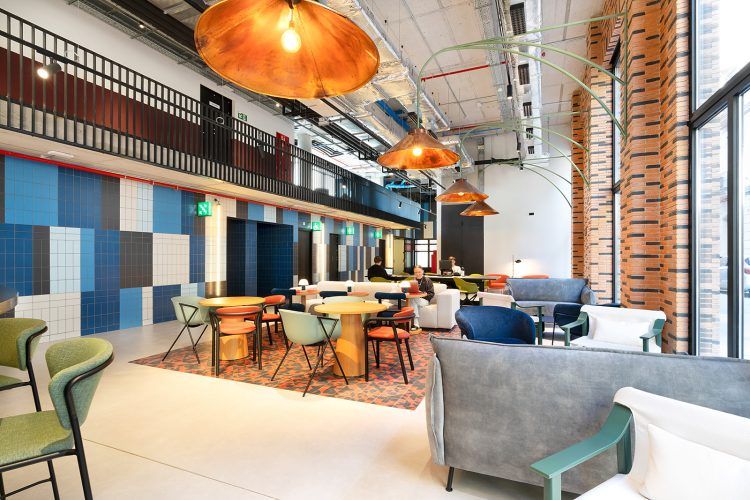 Salón moderno con sillas, mesas y sofás de colores, y lámparas de cobre colgantes.