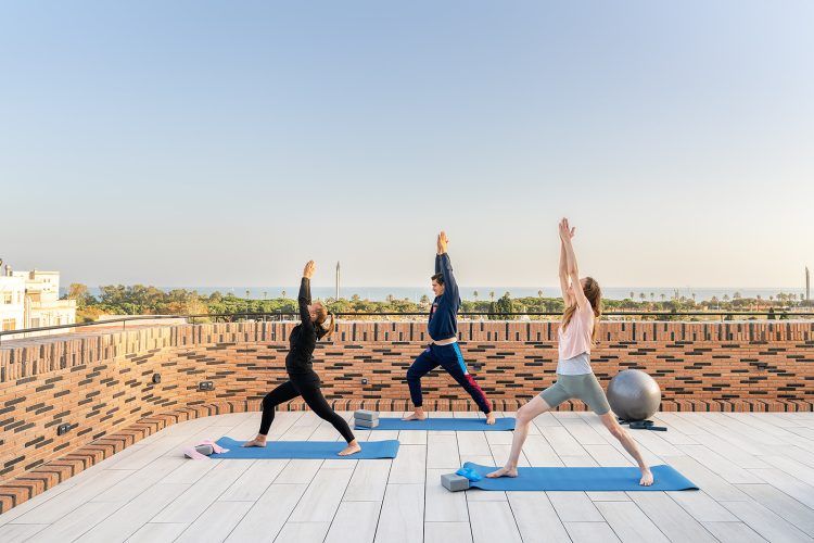 Tres personas haciendo poses de yoga en esterillas azules al aire libre