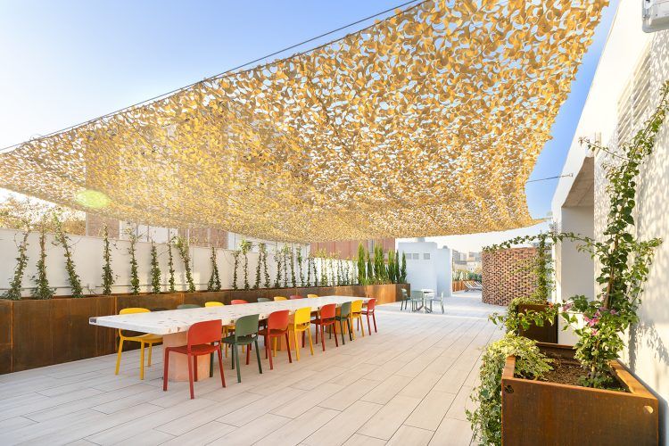 Terraza exterior con una mesa larga, sillas coloridas y una marquesina con un diseño en la parte superior.
